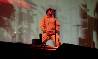 Anderson .Paak canta de moletom laranja, com microfone no pedestal, em show de dezembro de 2018