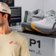 Modelo de boné e camiseta da coleção Asics Senna ao lado do tênis Novablast 6 em pódio com a marcação P1