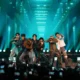 Os sete integrantes do BTS se apresentam em palco iluminado de verde diante do público