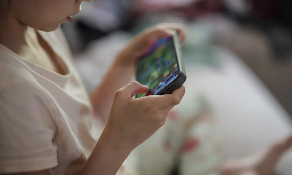 Mãos de criança segurando smartphone, imagem ilustrativa