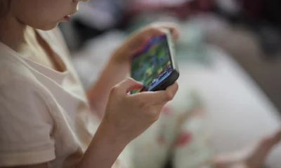Mãos de criança segurando smartphone, imagem ilustrativa