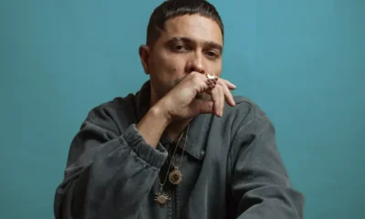 Don L com as mãos juntas diante do rosto em retrato de divulgação com fundo azul