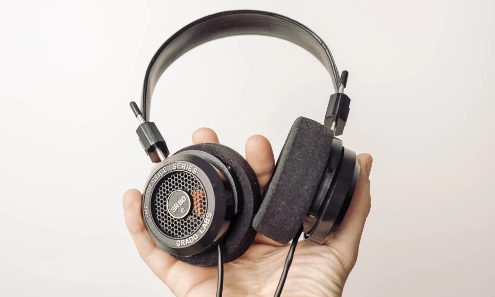 Mão segura fones de ouvido sobre fundo claro, imagem ilustrativa de streaming de música