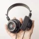 Mão segura fones de ouvido sobre fundo claro, imagem ilustrativa de streaming de música