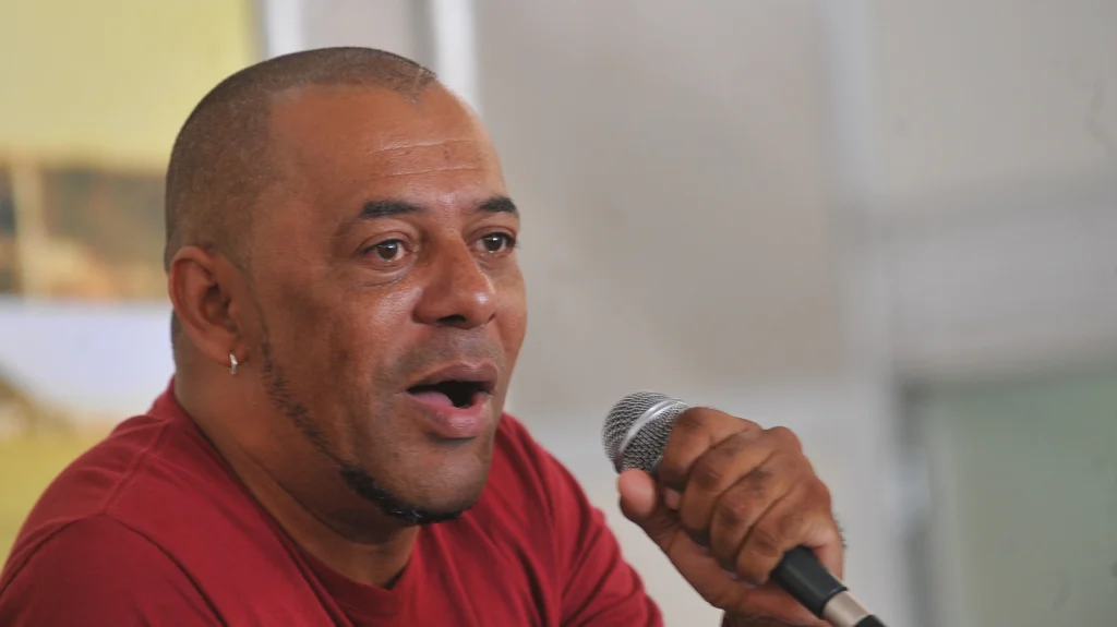 O rapper GOG, de camiseta vermelha, fala ao microfone em debate em Brasília