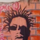 Grafite com o rosto do rapper Sabotage pintado sobre tijolos laranja, com letras cor-de-rosa