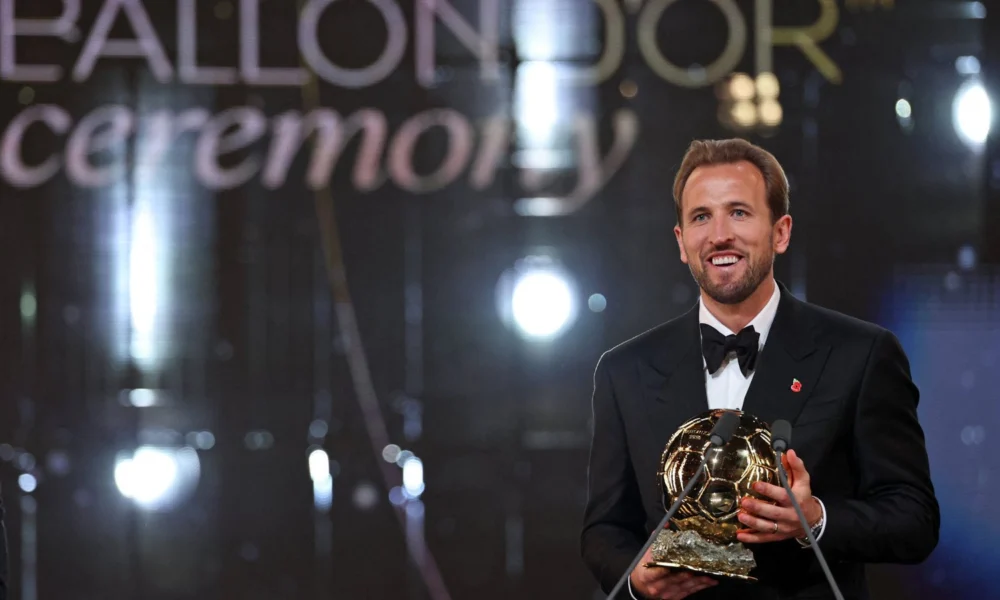 Harry Kane de smoking segura o troféu da Bola de Ouro 2026 no palco do Palladium, em Londres