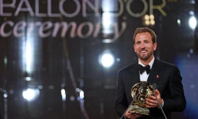 Harry Kane de smoking segura o troféu da Bola de Ouro 2026 no palco do Palladium, em Londres