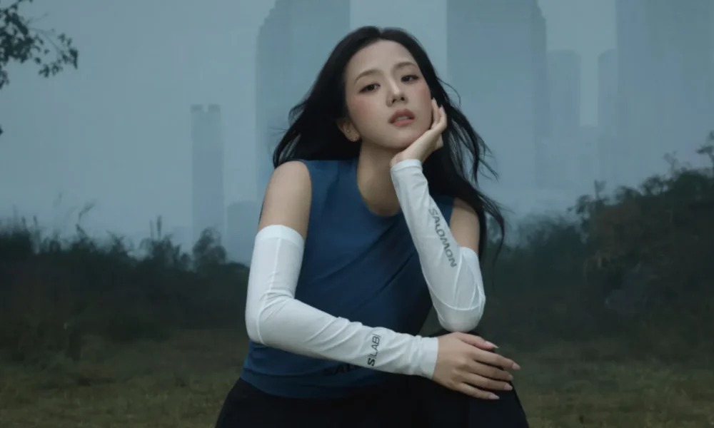 JISOO sentada em gramado com prédios de Seul ao fundo na campanha In The Open da Salomon