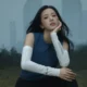 JISOO sentada em gramado com prédios de Seul ao fundo na campanha In The Open da Salomon