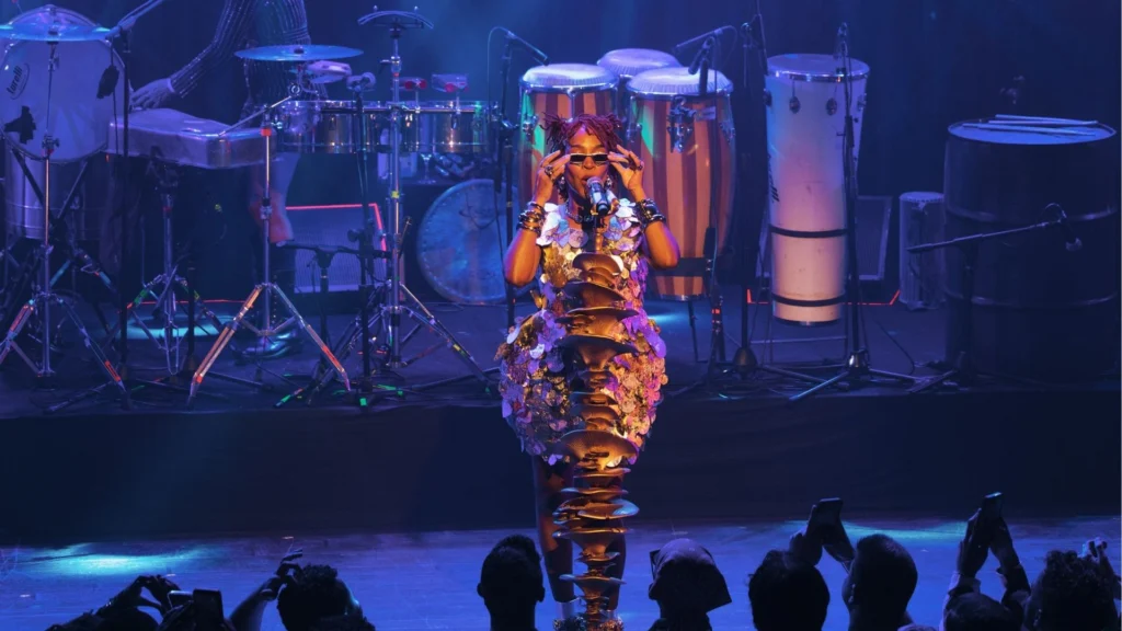 Karol Conká canta no palco com figurino dourado e banda de percussão ao fundo