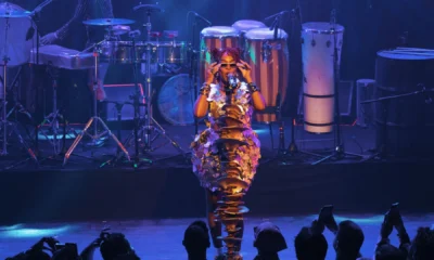 Karol Conká canta no palco com figurino dourado e banda de percussão ao fundo