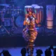 Karol Conká canta no palco com figurino dourado e banda de percussão ao fundo