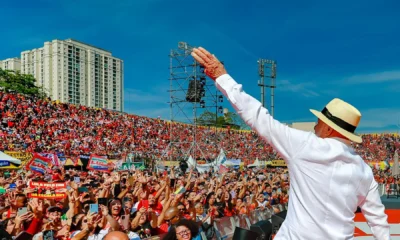 Lula, de chapéu e camisa branca, acena para multidão de apoiadores no lançamento da campanha de 2026