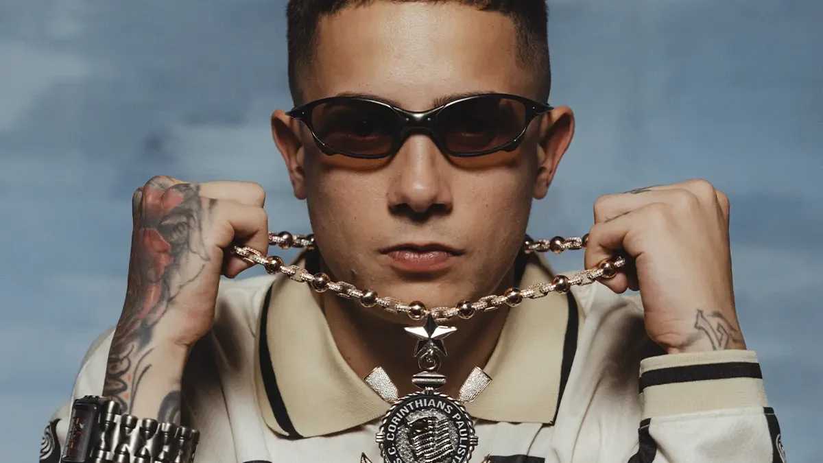 MC Hariel de óculos escuros segura corrente com pingente em foto de divulgação do novo EP