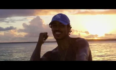 MC Livinho de boné azul em praia ao pôr do sol no clipe de Azul Piscina 2