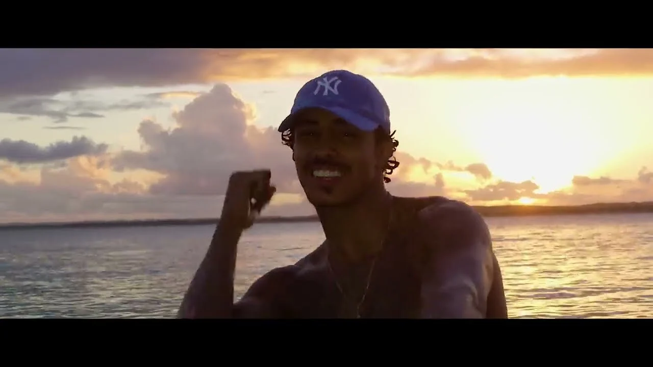 MC Livinho de boné azul em praia ao pôr do sol no clipe de Azul Piscina 2