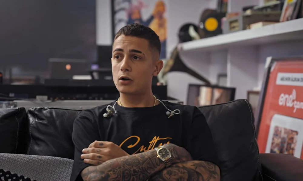 MC Hariel dá entrevista sentado em sofá em cena do documentário Melhores Dias