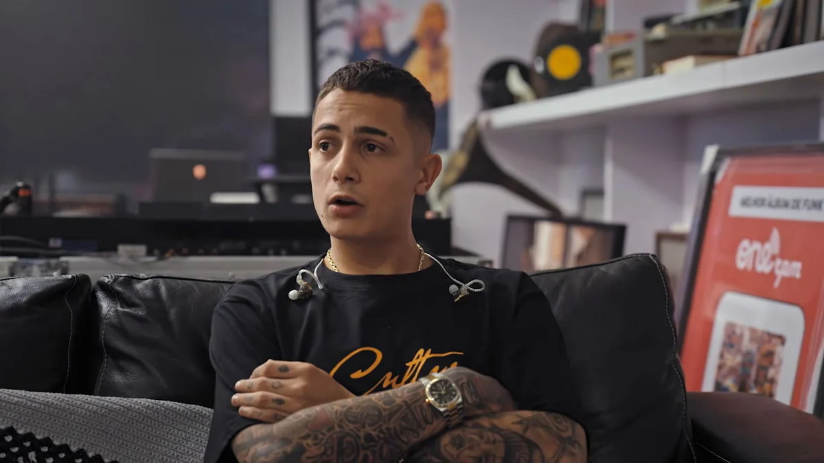 MC Hariel dá entrevista sentado em sofá em cena do documentário Melhores Dias