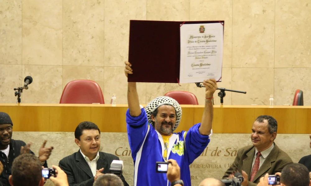 Nelson Triunfo, de touca de crochê e agasalho azul, ergue o diploma de Cidadão Paulistano na Câmara Municipal de São Paulo