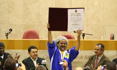 Nelson Triunfo, de touca de crochê e agasalho azul, ergue o diploma de Cidadão Paulistano na Câmara Municipal de São Paulo