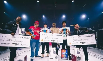 Neo BXD de camisa listrada vermelha e preta entra no palco de uma batalha de rima