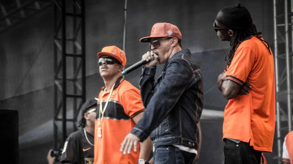 Integrantes dos Racionais MC's no palco da Virada Cultural de São Paulo, com camisas laranja e jaqueta jeans
