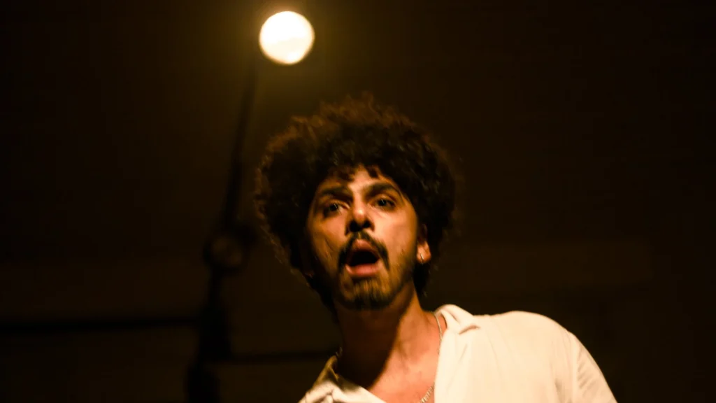 O ator Rafael Cristiano, de camisa branca, em cena sob luz baixa no espetáculo do Grupo II