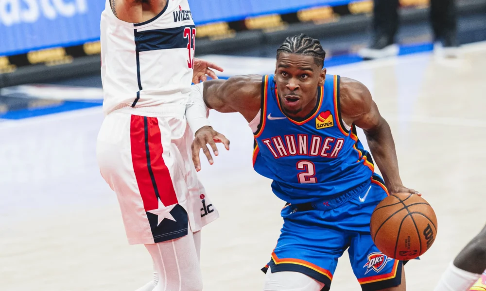 Shai Gilgeous-Alexander com o uniforme azul do Oklahoma City Thunder conduzindo a bola em jogo da NBA