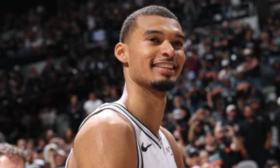 Victor Wembanyama sorri em quadra com o uniforme branco do San Antonio Spurs