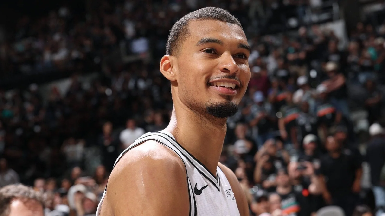Victor Wembanyama sorri em quadra com o uniforme branco do San Antonio Spurs