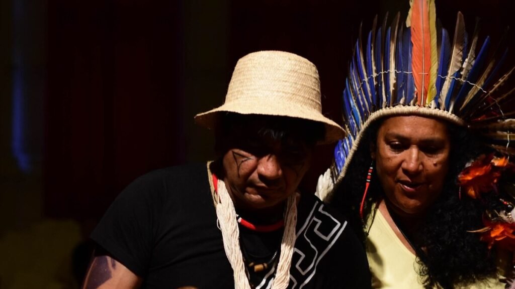 Duas pessoas indígenas com adornos tradicionais em atividade cultural; imagem de divulgação da Virada Indígena 2026.